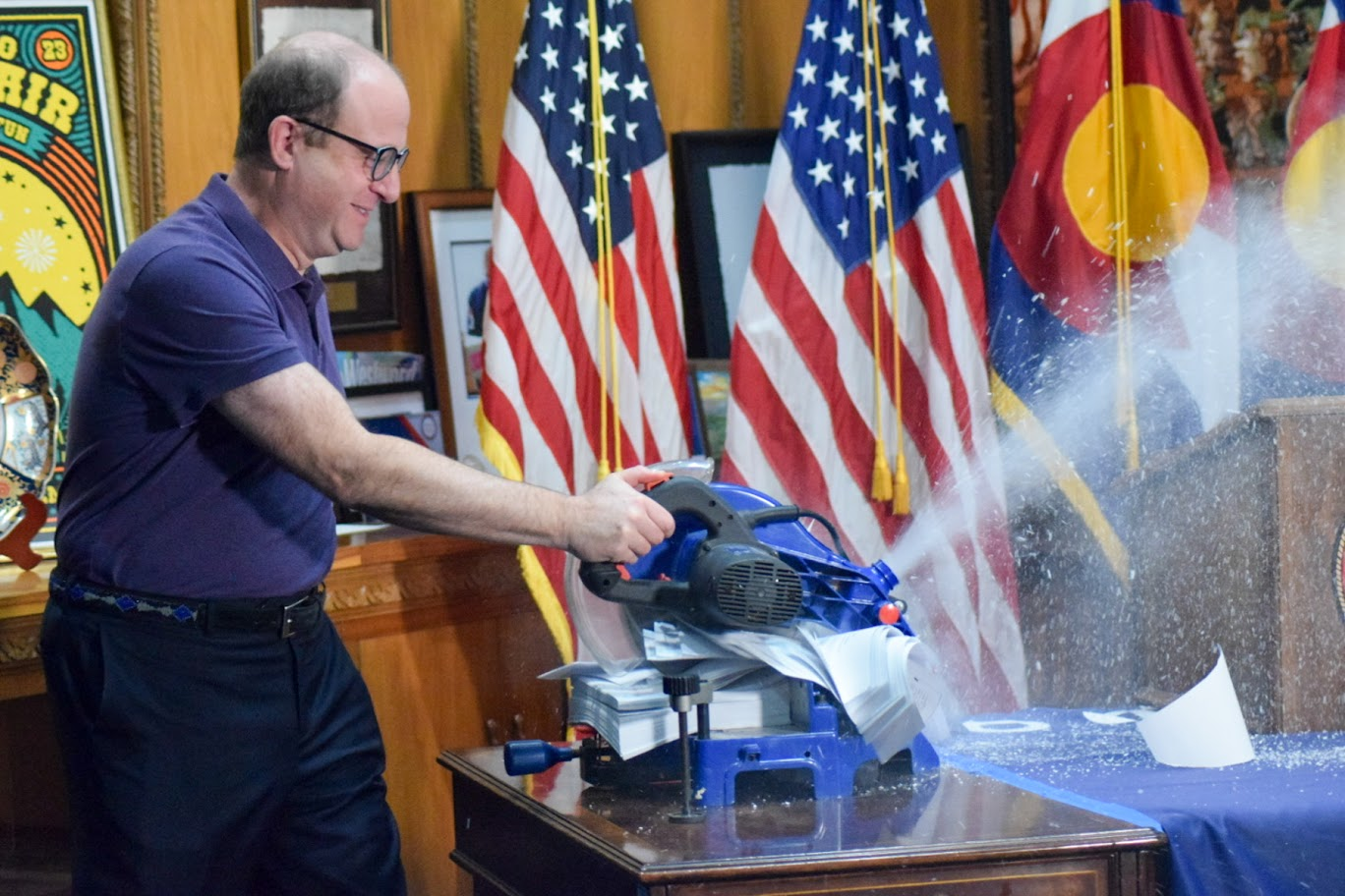 Governor Polis cutting though 208 executive orders with a chop saw after he rescinded them. 